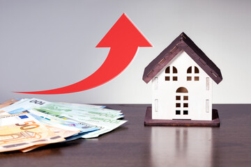 House, property or real estate market price go up or rising concept. Model of house and  euro bills on desk with red up arrow.