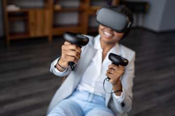 Happy young african american woman office employee in 3D goggles playing VR games, relaxed black businesswoman with gaming controllers in hands imitating movements in virtual reality. Selective focus