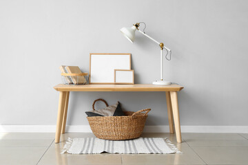 Fototapeta na wymiar Table with white lamp, books and frames near light wall