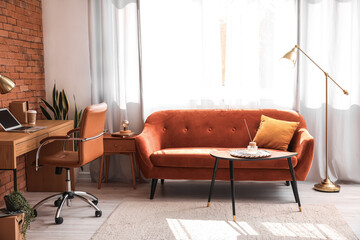Interior of stylish living room with red sofa, workplace and golden lamp