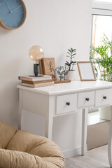 Stylish lamp, books, frame and flowerpot on table near light wall