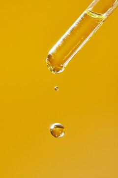 A drop of cosmetic aromatic oil drips from the pipette. Front view.