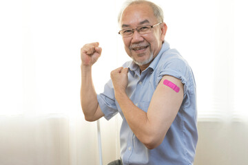 Portrait of an elderly asian man smiling after receiving the vaccine. A mature man shows his arm with a bandage after full vaccination.