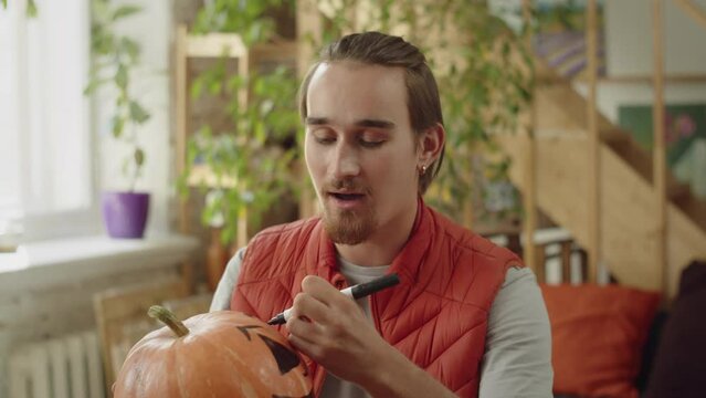 A young man is painting over the pumpkin's eyes