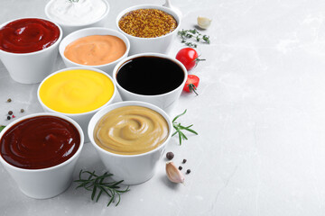 Many bowls with different sauces on light grey table, space for text