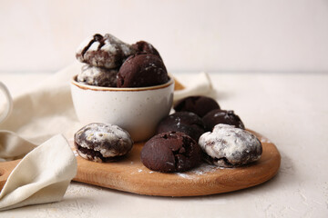 Wooden board and bowl of chocolate brownie cookies on light background