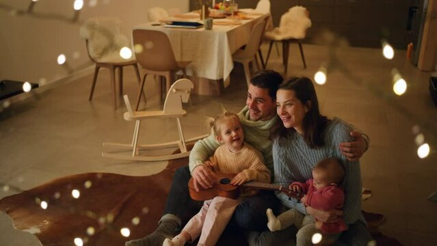 Happy young family with small children sitting on floor and playing the guitar in cabin on holiday.