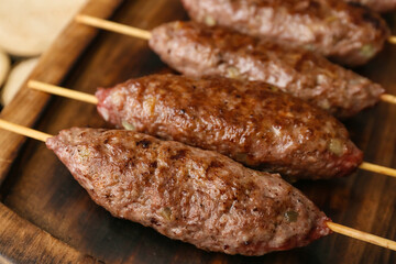 Wooden board of skewers with tasty lula kebab on table, closeup