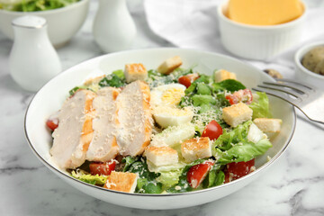 Delicious Caesar salad in bowl on white marble table, closeup