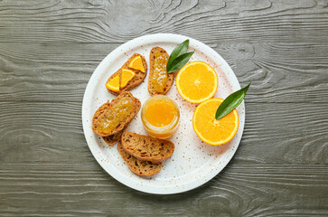Plate with tasty orange jam and bread on wooden background