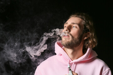 Vaping young man on black background