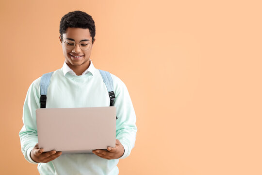 Male African-American student with modern laptop on color background