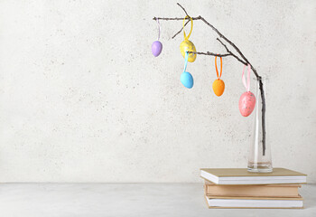 Books, vase with tree branch and different Easter eggs on light background