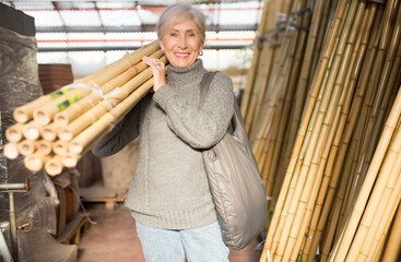 Senior woman carrying bunch of bamboo poles while shopping in home goods store.