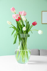 Vase with beautiful tulip flowers on dining table in room