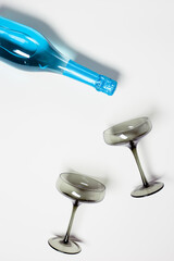 Blue Champagne or sparkling wine poured from bottle with glasses tinted grey glass, creative flat lay, summer drink concept. Modern colored glasses for wine or champagne on white background