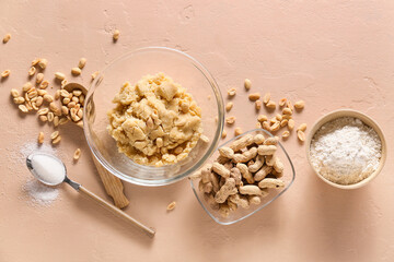 Bowl with fresh dough and ingredients for preparing peanut cookies on beige background