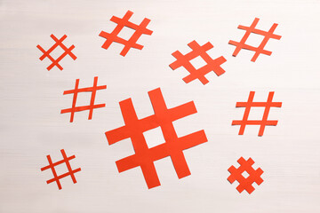 Obraz premium Red paper cutout symbols of hashtag on white wooden background, flat lay