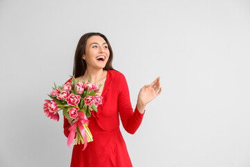 Beautiful happy young woman with bouquet of flowers on light background. International Women's Day celebration