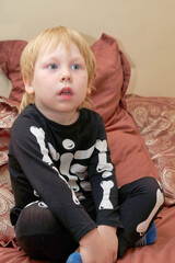 A child in a skeleton costume sits on the couch with an emotion on his face - 487498901