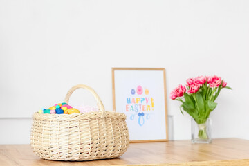 Fototapeta na wymiar Basket with Easter eggs on table near light wall