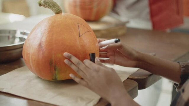 A young lady is drawing eyes and a mouth on a halloween pumpkin