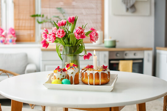 Tray with Easter cakes, eggs and vase with tulips on dining table