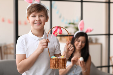 Little boy in bunny ears holding basket with Easter eggs at home