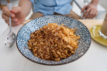 Bowl with granules and coconut and chocolate chips for a healthy breakfast. Male hand with a spoon and a plate with muesli