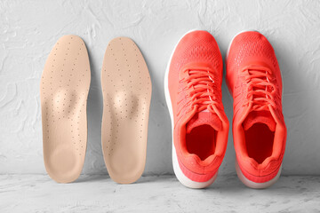 Orthopedic insoles and sneakers on light background