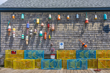 The gray plank wall of a traditional home is adorned with old floats and lobster traps as a symbol of a New England fishing village by the Atlantic Ocean.