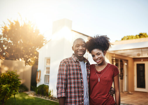 Proud first-time homeowners. Portrait of a young couple standing outside in front of their new house.