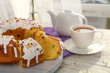 Board with pieces of tasty Easter cake and cup of tea on light wooden table, closeup