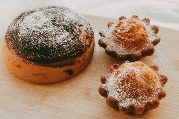 cupcakes and a bun with chocolate sprinkled with powdered sugar on a wooden background