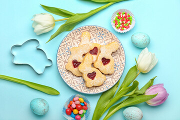 Plate with delicious Easter cookies and tulip flowers on blue background