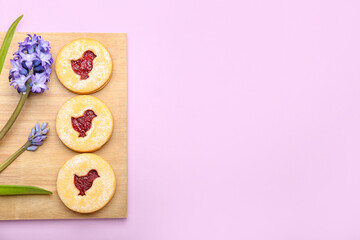 Board with delicious Easter cookies and flowers on purple background