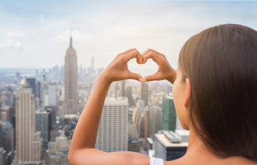 New York Tourist doing heart shape with hands gesture at NYC skyline view from rooftop. View from behind, USA Travel vacation destination.