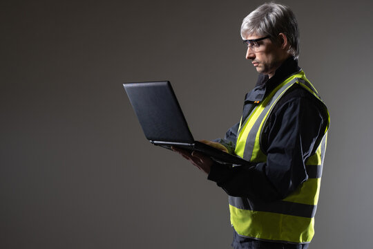 Laptop engineer. Experienced engineer. Gray-haired man in yellow vest. Portrait of engineer on studio background. Man is holding open laptop. Engineering software concept. Builder or architect - Powered by Adobe