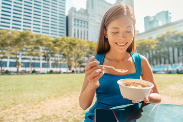 Healthy food Asian woman eating Acai bowl breakfast with spoon at New York City park on morning or...