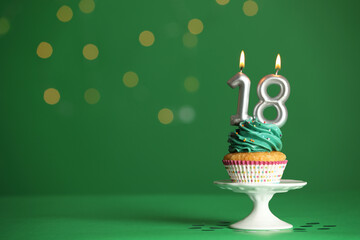 Coming of age party - 18th birthday. Delicious cupcake with number shaped candles on green...