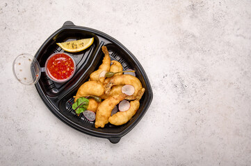 Top view tempura shrimp with sweet sour chili sauce and radishes in black plastic container on light background. Designer food concept for take away or delivery