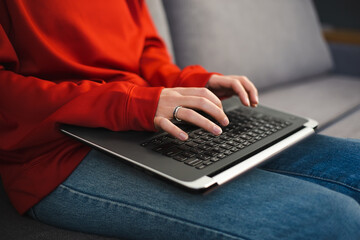 Freelancer girl working on laptop computer at home during lockdown. Young woman in red hoodie shirt typing text on modern notebook pc. Entrepreneur person doing distant work online