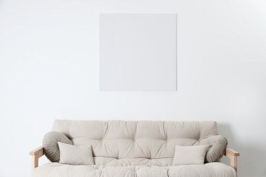 Blank canvas on wall over beige sofa indoors. Space for design