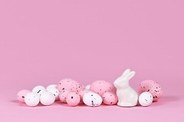 White and pink Easter eggs with small bunny sculpture on pink background with copy space