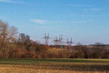 High voltage poles for electricity distribution in the countryside. In the background is a blue sky with dramatic clouds.