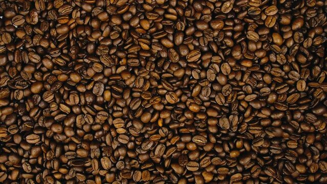 The coffee beans spin rotate quickly fast fly, dispart, splash to the sides with centrifugal coriolis force. The video is in reverse. Coffee beans twist, create pattern, make design figure picture.