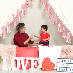 Latina mom and daughter show their love under a teepee with a sign that says 