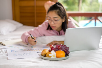 Obraz na płótnie Canvas work from home, a young Asian woman who works in finance at home calculates financial graphs showing the results of his investments, planning the steps of his business growth
