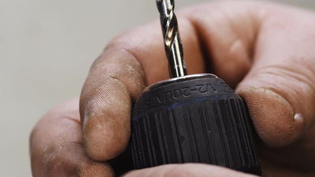 Mans hand inserted drill bit into screwdriver and fixed, closeup. Male fingers insert drill into construction tool and twist it
