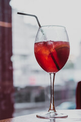 Vertical image of wine glass of alcoholic cold drink cocktail beverage juice with black plastic straw. Drops of condensation. Blurred background cafe bar restaurant window. Close up
